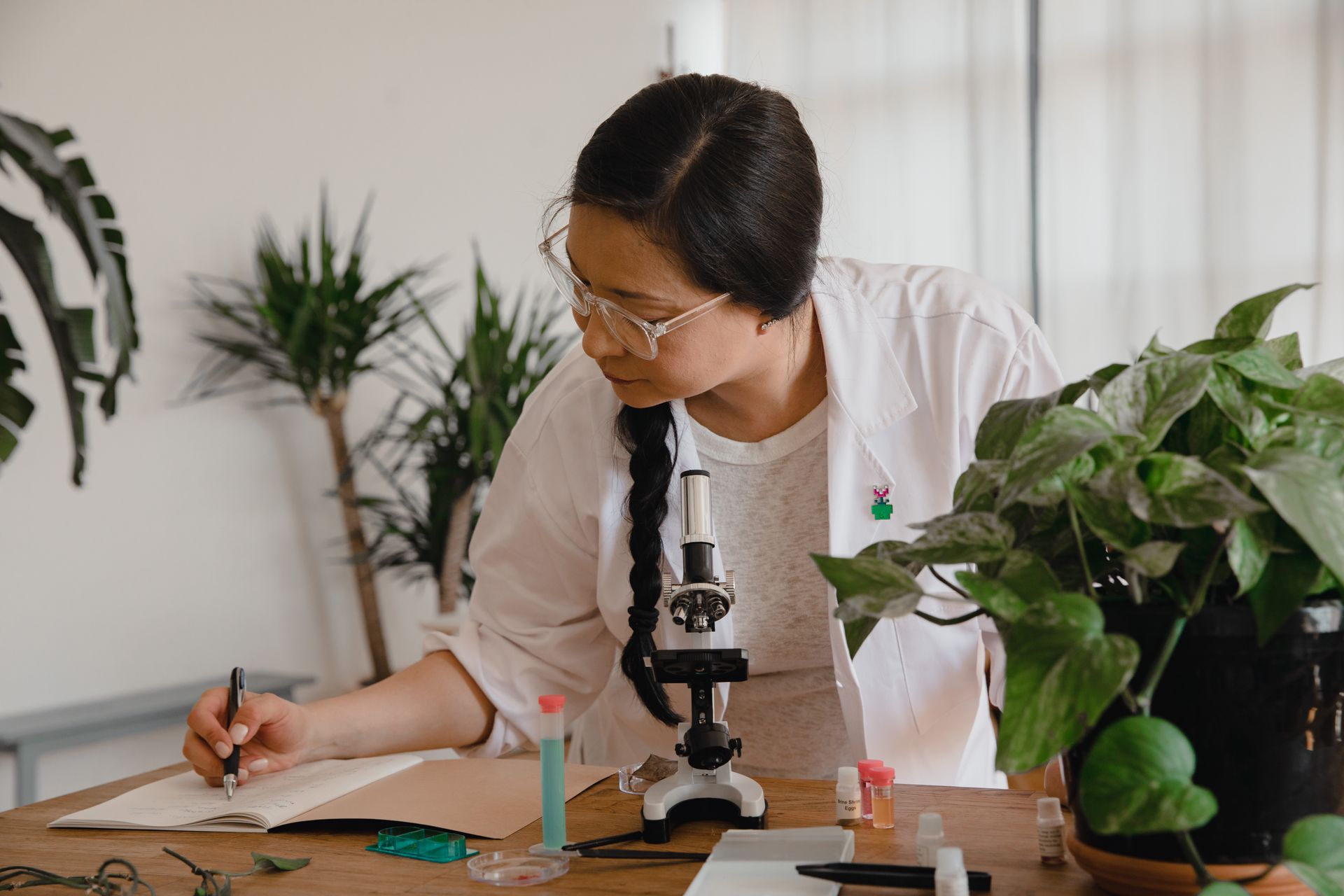 Researcher taking notes beside a microscope and plants